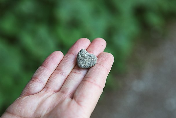 Ein kleiner Stein in Herzform liegt auf einer Hand.