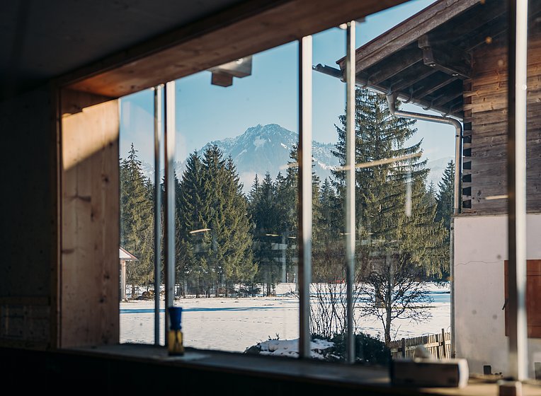 Blick durchs Fenster in die verschneite Landschaft mit Fichten und Berg