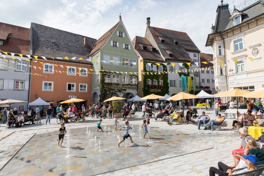 Kinder rennen durchs Wasserspiel auf dem geschmückten, lebendigen Marktplatz, mitten in der Altstadt von Isny.