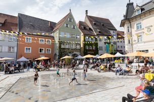 Kinder rennen durchs Wasserspiel auf dem geschmückten, lebendigen Marktplatz, mitten in der Altstadt von Isny.