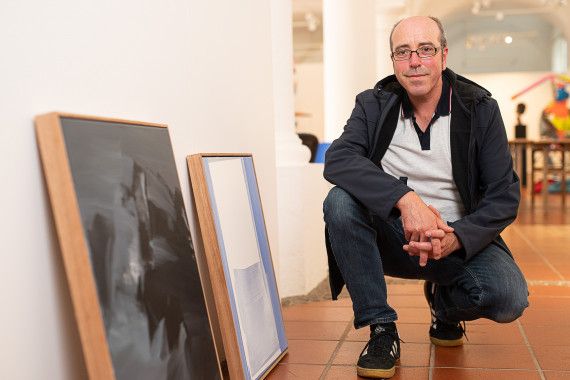 Stefan Winkler neben seinen prämierten Werken "Berglandschaft" und "Abstrakt (weiss)" 2021 im Hofgartensaal der Residenz Kempten